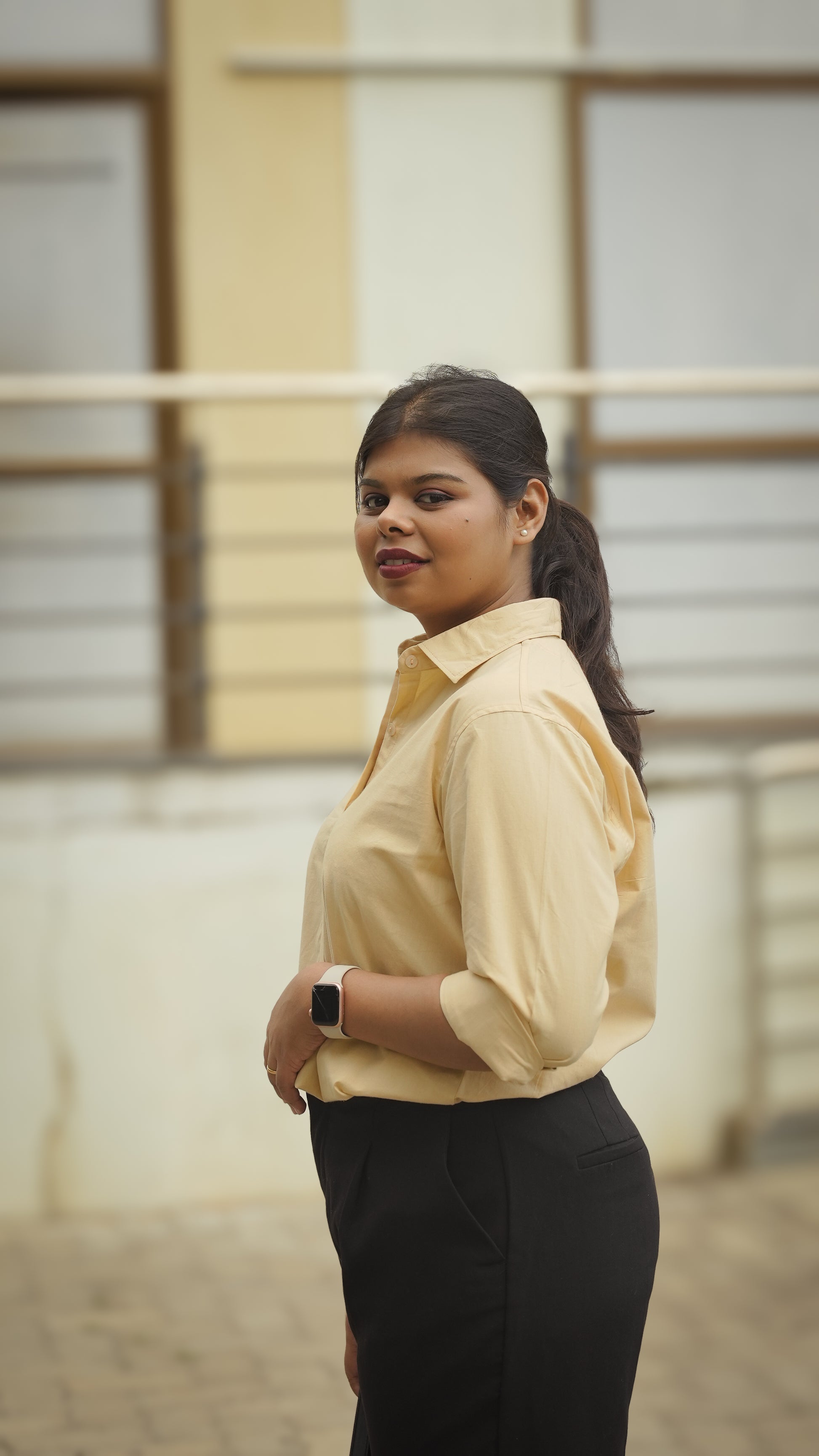 Woman wearing a beige shirt and black pants standing outdoors.